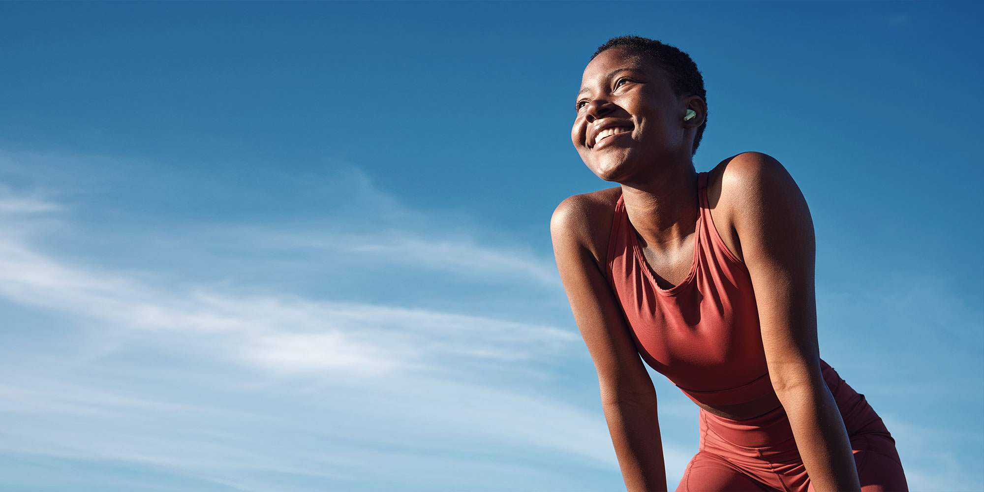 woman and happy athlete smile after running, exercise and marathon training workout. Blue sky, summer sports
