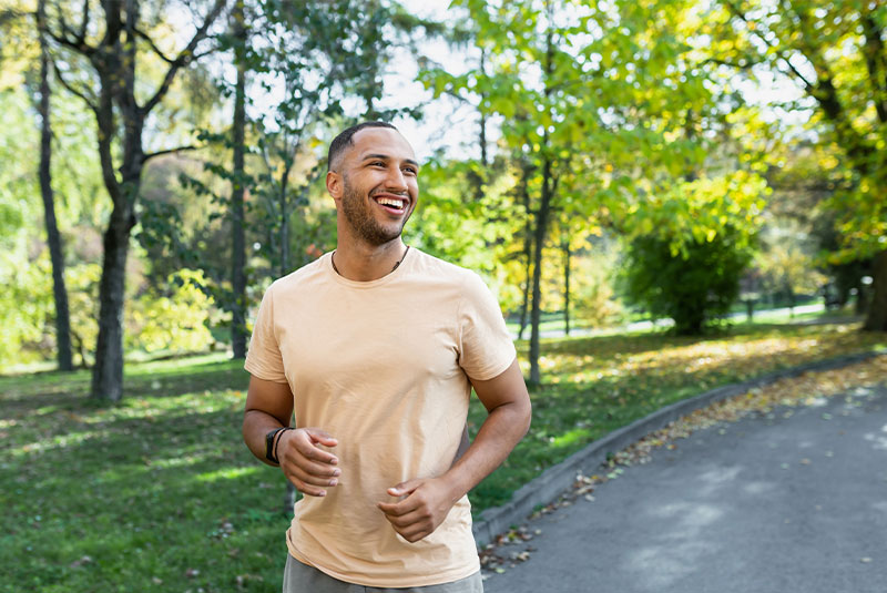 Cheerful and successful hispanic man jogging in the park, man running on a sunny day, smiling and happy having an outdoor activity